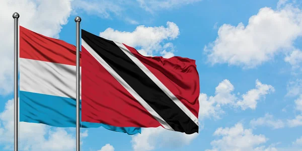 Luxemburgo e Trinidad e Tobago acenando com o vento contra o céu azul nublado branco juntos. Conceito de diplomacia, relações internacionais . — Fotografia de Stock