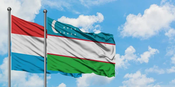 Bandera de Luxemburgo y Uzbekistán ondeando en el viento contra el cielo azul nublado blanco juntos. Concepto diplomático, relaciones internacionales . — Foto de Stock