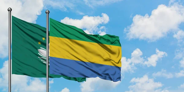 Макао і Габон прапор розмахував вітром проти білого хмарного синього неба разом. Концепція дипломатії, міжнародні відносини. — стокове фото