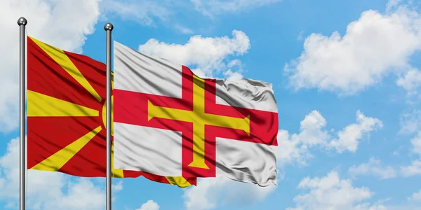 Bandera de Macedonia y Guernsey ondeando en el viento contra el cielo azul nublado blanco juntos. Concepto diplomático, relaciones internacionales . — Foto de Stock