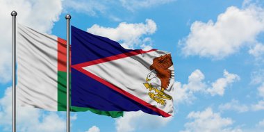 Madagaskar ve Amerikan Samoası bayrağı birlikte beyaz bulutlu mavi gökyüzüne karşı rüzgarda sallayarak. Diplomasi kavramı, uluslararası ilişkiler.
