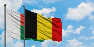 Madagaskar ve Belçika bayrağı birlikte beyaz bulutlu mavi gökyüzüne karşı rüzgarda sallayarak. Diplomasi kavramı, uluslararası ilişkiler.