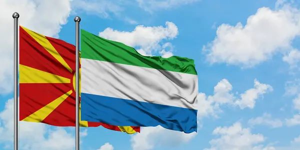 Bandera de Macedonia y Sierra Leona ondeando en el viento contra el cielo azul nublado blanco juntos. Concepto diplomático, relaciones internacionales . — Foto de Stock