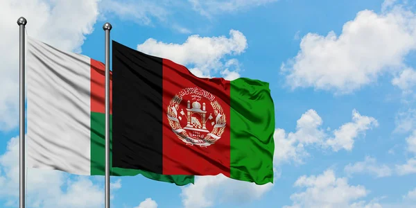 Bandera de Madagascar y Afganistán ondeando en el viento contra el cielo azul nublado blanco juntos. Concepto diplomático, relaciones internacionales . — Foto de Stock