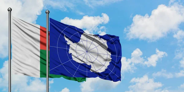 Bandera de Madagascar y la Antártida ondeando en el viento contra el cielo azul nublado blanco juntos. Concepto diplomático, relaciones internacionales . — Foto de Stock