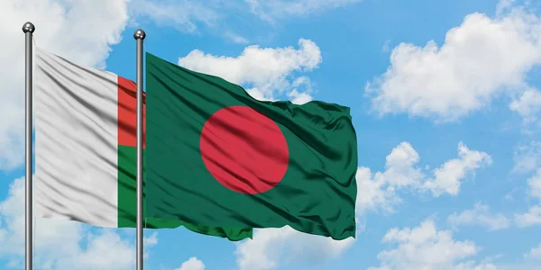 Bandera de Madagascar y Bangladesh ondeando en el viento contra el cielo azul nublado blanco juntos. Concepto diplomático, relaciones internacionales . — Foto de Stock