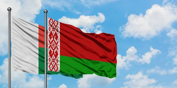 Bandera de Madagascar y Bielorrusia ondeando en el viento contra el cielo azul nublado blanco juntos. Concepto diplomático, relaciones internacionales . — Foto de Stock