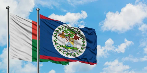 Bandera de Madagascar y Belice ondeando en el viento contra el cielo azul nublado blanco juntos. Concepto diplomático, relaciones internacionales . — Foto de Stock