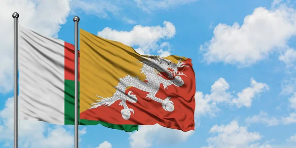 Madagaskar en Bhutan vlag zwaaien in de wind tegen witte bewolkte blauwe hemel samen. Diplomatie concept, internationale betrekkingen. — Stockfoto