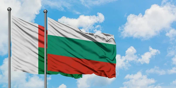 Bandera de Madagascar y Bulgaria ondeando en el viento contra el cielo azul nublado blanco juntos. Concepto diplomático, relaciones internacionales . — Foto de Stock