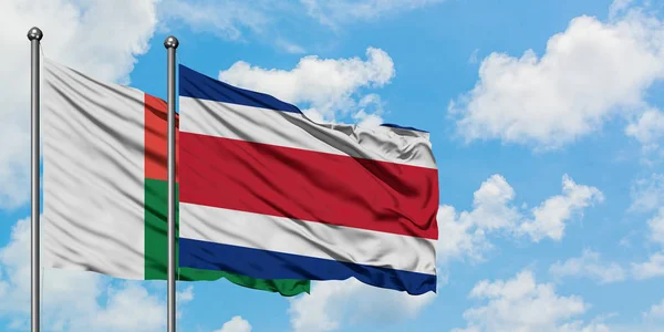 Madagascar e Costa Rica sventolano insieme la bandiera contro il bianco cielo azzurro nuvoloso. Concetto di diplomazia, relazioni internazionali . — Foto Stock
