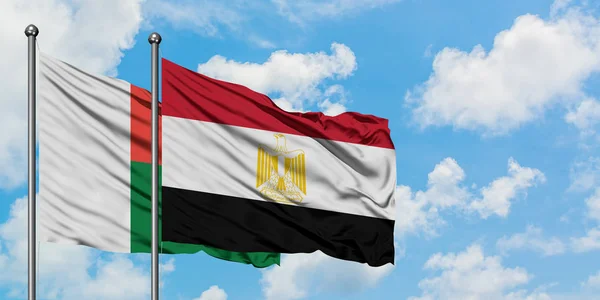 Bandera de Madagascar y Egipto ondeando en el viento contra el cielo azul nublado blanco juntos. Concepto diplomático, relaciones internacionales . — Foto de Stock