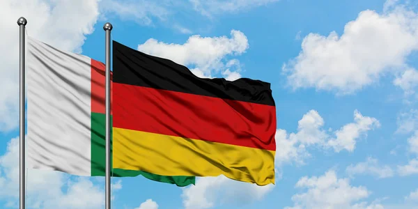 Madagáscar e a bandeira da Alemanha agitando no vento contra o céu azul nublado branco juntos. Conceito de diplomacia, relações internacionais . — Fotografia de Stock