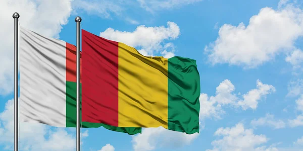 Madagaskar i Gwinea flaga machając w wiatr przed białym zachmurzone błękitne niebo razem. Koncepcja dyplomacji, stosunki międzynarodowe. — Zdjęcie stockowe