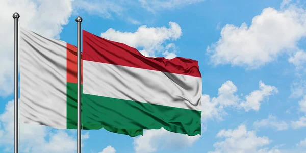 Madagaszkár és Magyarország zászlója integetett a szél ellen, a fehér felhős kék ég együtt. Diplomáciai koncepció, nemzetközi kapcsolatok. — Stock Fotó