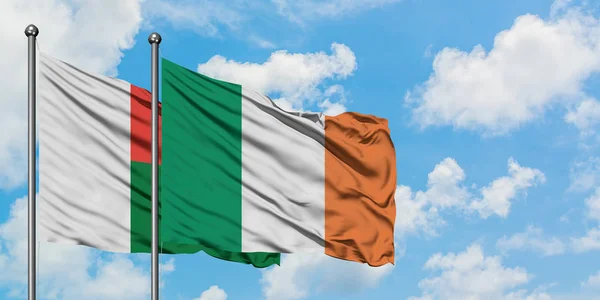 Η σημαία της Μαδαγασκάρης και της Ιρλανδίας κουνώντας τον άνεμο ενάντια στον λευκό νεφελώδες γαλάζιο ουρανό μαζί. Φιλοσοφία της διπλωματίας, διεθνείς σχέσεις. — Φωτογραφία Αρχείου