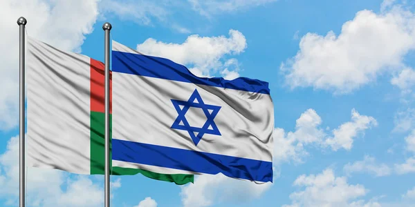 Madagaskar en Israël vlag zwaaien in de wind tegen witte bewolkte blauwe hemel samen. Diplomatie concept, internationale betrekkingen. — Stockfoto