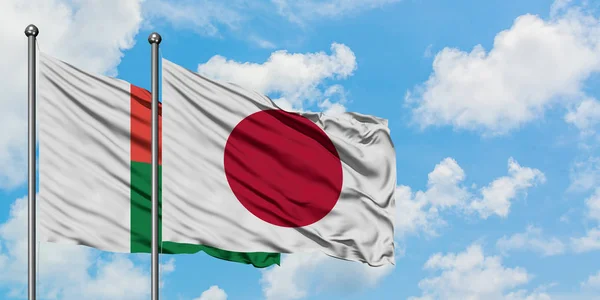 Bandera de Madagascar y Japón ondeando en el viento contra el cielo azul nublado blanco juntos. Concepto diplomático, relaciones internacionales . — Foto de Stock