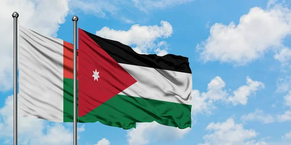 Madagaskar und jordanische Flagge wehen gemeinsam im Wind vor dem wolkenverhangenen blauen Himmel. Diplomatie-Konzept, internationale Beziehungen. — Stockfoto