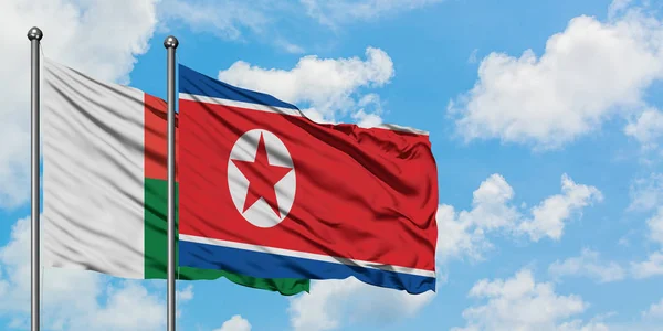 Bandera de Madagascar y Corea del Norte ondeando en el viento contra el cielo azul nublado blanco juntos. Concepto diplomático, relaciones internacionales . — Foto de Stock