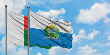 Madagaskar ve San Marino bayrağı birlikte beyaz bulutlu mavi gökyüzüne karşı rüzgarda sallayarak. Diplomasi kavramı, uluslararası ilişkiler.