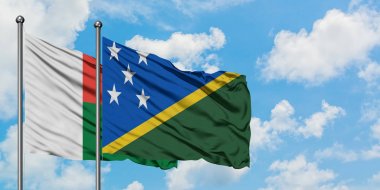 Madagaskar ve Solomon Adaları bayrağı birlikte beyaz bulutlu mavi gökyüzüne karşı rüzgarda sallayarak. Diplomasi kavramı, uluslararası ilişkiler.