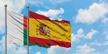 Madagaskar ve İspanya bayrağı birlikte beyaz bulutlu mavi gökyüzüne karşı rüzgarda sallayarak. Diplomasi kavramı, uluslararası ilişkiler.