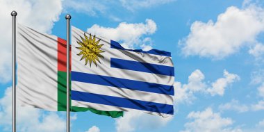 Madagaskar ve Uruguay bayrağı birlikte beyaz bulutlu mavi gökyüzüne karşı rüzgarda sallayarak. Diplomasi kavramı, uluslararası ilişkiler.
