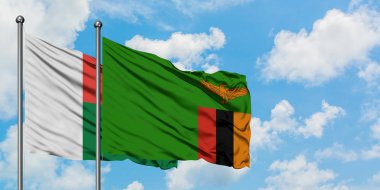 Madagaskar ve Zambiya bayrağı birlikte beyaz bulutlu mavi gökyüzüne karşı rüzgarda sallayarak. Diplomasi kavramı, uluslararası ilişkiler.