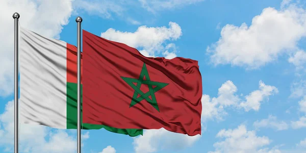 Drapeau de Madagascar et du Maroc agitant dans le vent contre ciel bleu nuageux blanc ensemble. Concept de diplomatie, relations internationales . — Photo