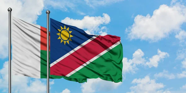 Drapeau de Madagascar et de Namibie agitant dans le vent contre ciel bleu nuageux blanc ensemble. Concept de diplomatie, relations internationales . — Photo