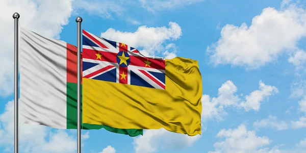 Bandera de Madagascar y Niue ondeando en el viento contra el cielo azul nublado blanco juntos. Concepto diplomático, relaciones internacionales . — Foto de Stock