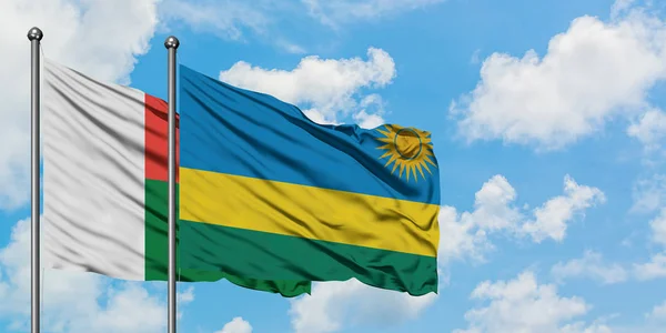 Bandera de Madagascar y Ruanda ondeando en el viento contra el cielo azul nublado blanco juntos. Concepto diplomático, relaciones internacionales . — Foto de Stock