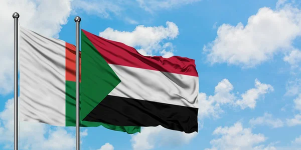 Bandera de Madagascar y Sudán ondeando en el viento contra el cielo azul nublado blanco juntos. Concepto diplomático, relaciones internacionales . — Foto de Stock