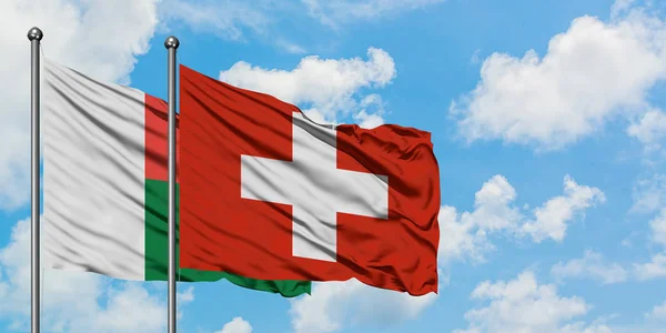 Прапор Мадагаскару і Швейцарії розмахував вітром проти білого хмарного синього неба разом. Концепція дипломатії, міжнародні відносини. — стокове фото