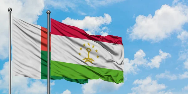 Bandera de Madagascar y Tayikistán ondeando en el viento contra el cielo azul nublado blanco juntos. Concepto diplomático, relaciones internacionales . — Foto de Stock