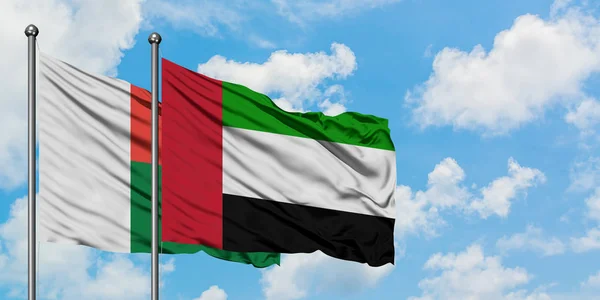 Madagascar y los Emiratos Árabes Unidos ondean en el viento contra el cielo azul nublado blanco juntos. Concepto diplomático, relaciones internacionales . — Foto de Stock