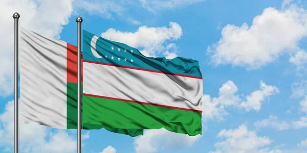 Bandera de Madagascar y Uzbekistán ondeando en el viento contra el cielo azul nublado blanco juntos. Concepto diplomático, relaciones internacionales . —  Fotos de Stock