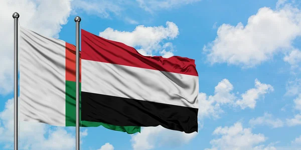 Bandera de Madagascar y Yemen ondeando en el viento contra el cielo azul nublado blanco juntos. Concepto diplomático, relaciones internacionales . — Foto de Stock