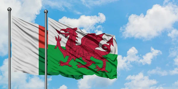 Η σημαία της Μαδαγασκάρης και της Ουαλίας κουνώντας τον άνεμο ενάντια στον λευκό θολό γαλάζιο ουρανό μαζί. Φιλοσοφία της διπλωματίας, διεθνείς σχέσεις. — Φωτογραφία Αρχείου