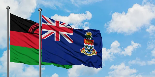 Bandera de Malawi y las Islas Caimán ondeando en el viento contra el cielo azul nublado blanco juntos. Concepto diplomático, relaciones internacionales . — Foto de Stock