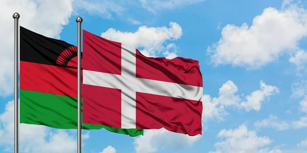 Vlajka Malawi a Dánska vlaje ve větru proti bíle zatažené modré obloze. Diplomacie, mezinárodní vztahy. — Stock fotografie