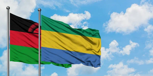 Bandera de Malawi y Gabón ondeando en el viento contra el cielo azul nublado blanco juntos. Concepto diplomático, relaciones internacionales . — Foto de Stock