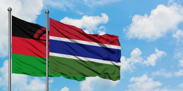 Bandera de Malawi y Gambia ondeando en el viento contra el cielo azul nublado blanco juntos. Concepto diplomático, relaciones internacionales . — Foto de Stock