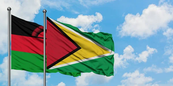 Bandera de Malawi y Guyana ondeando en el viento contra el cielo azul nublado blanco juntos. Concepto diplomático, relaciones internacionales . — Foto de Stock