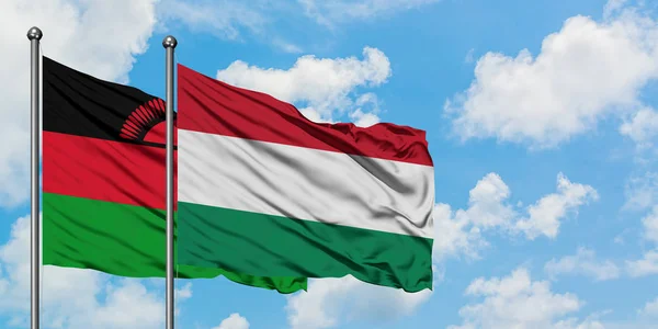 Bandera de Malawi y Hungría ondeando en el viento contra el cielo azul nublado blanco juntos. Concepto diplomático, relaciones internacionales . — Foto de Stock