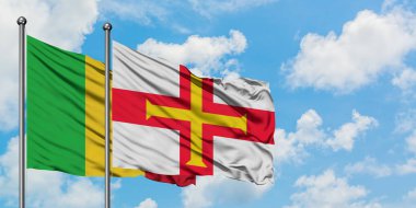 Mali ve Guernsey bayrağı birlikte beyaz bulutlu mavi gökyüzüne karşı rüzgarda sallayarak. Diplomasi kavramı, uluslararası ilişkiler.