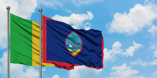 Bandera de Malí y Guam ondeando en el viento contra el cielo azul nublado blanco juntos. Concepto diplomático, relaciones internacionales . — Foto de Stock