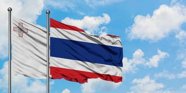 Malta e a bandeira da Tailândia agitando no vento contra o céu azul nublado branco juntos. Conceito de diplomacia, relações internacionais . — Fotografia de Stock