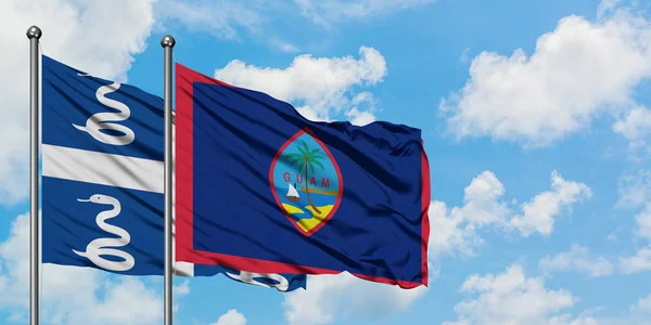 Martinica y la bandera de Guam ondeando en el viento contra el cielo azul nublado blanco juntos. Concepto diplomático, relaciones internacionales . — Foto de Stock